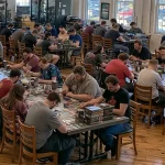 A group of card gamers playing on long tables in a brightly lit room